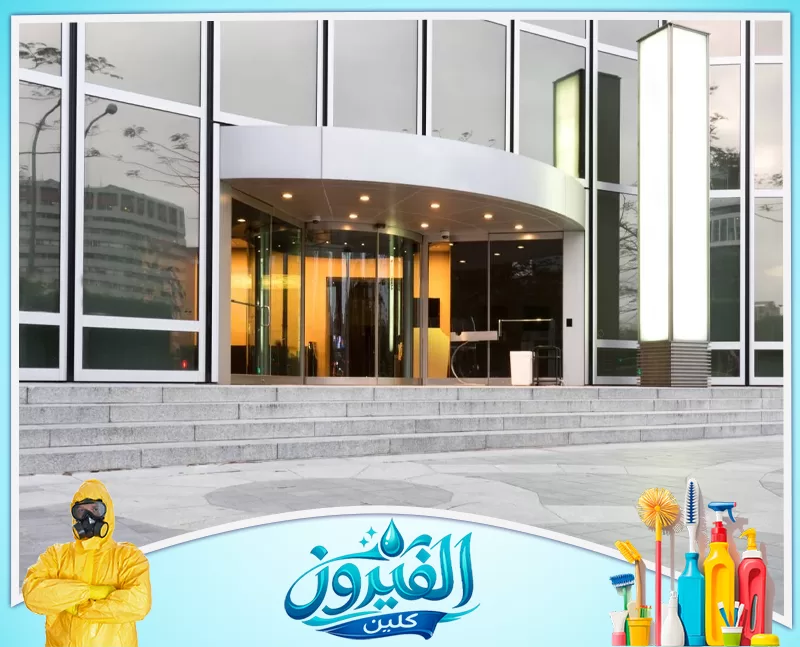 تنظيف مداخل العمائر في الجبيل 0562185880 شركة الفيروز مدخل مبنى حديث بواجهة زجاجية وباب دوار وإضاءة دافئة، تتقدمه درجات حجرية واسعة وتصميم معماري أنيق