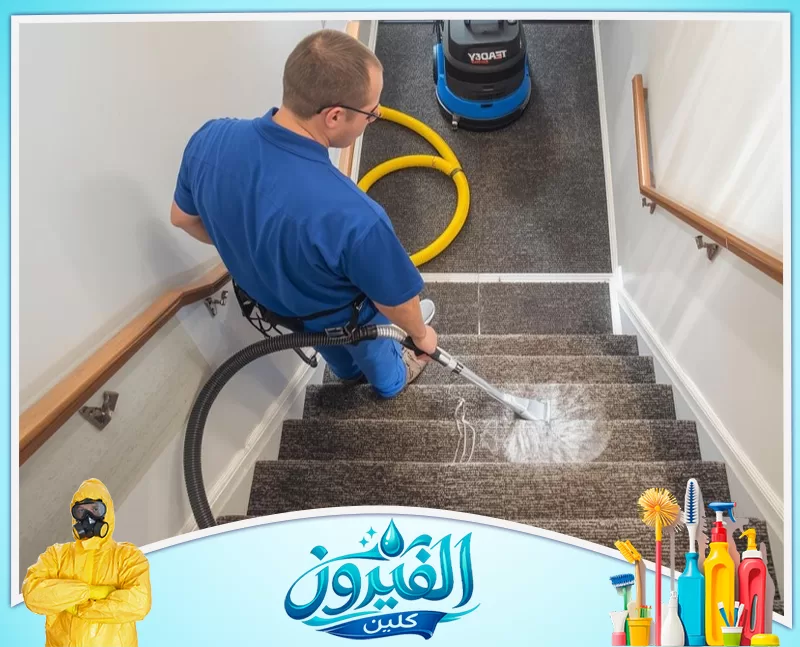تنظيف مداخل العمائر برأس تنورة 0562185880 شركة الفيروز عامل تنظيف يستخدم مكنسة كهربائية صناعية لتنظيف السجاد الرمادي على الدرج بعمق وإتقان.