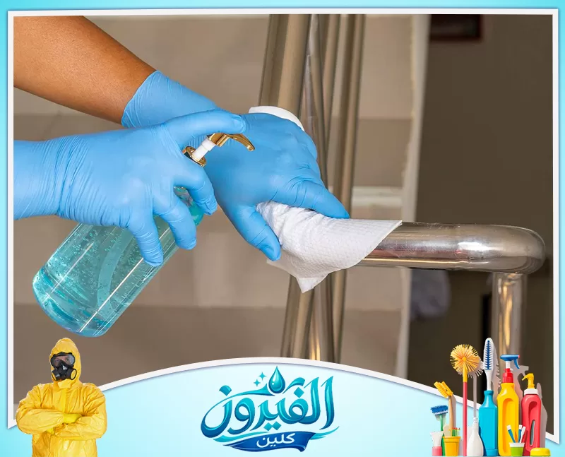 تنظيف الأبواب الزجاجية لمداخل العمائر 0562185880 شركة الفيروز شخص يرتدي قفازات زرقاء يستخدم جل معقم ومنديل ورقي لتنظيف درابزين معدني.