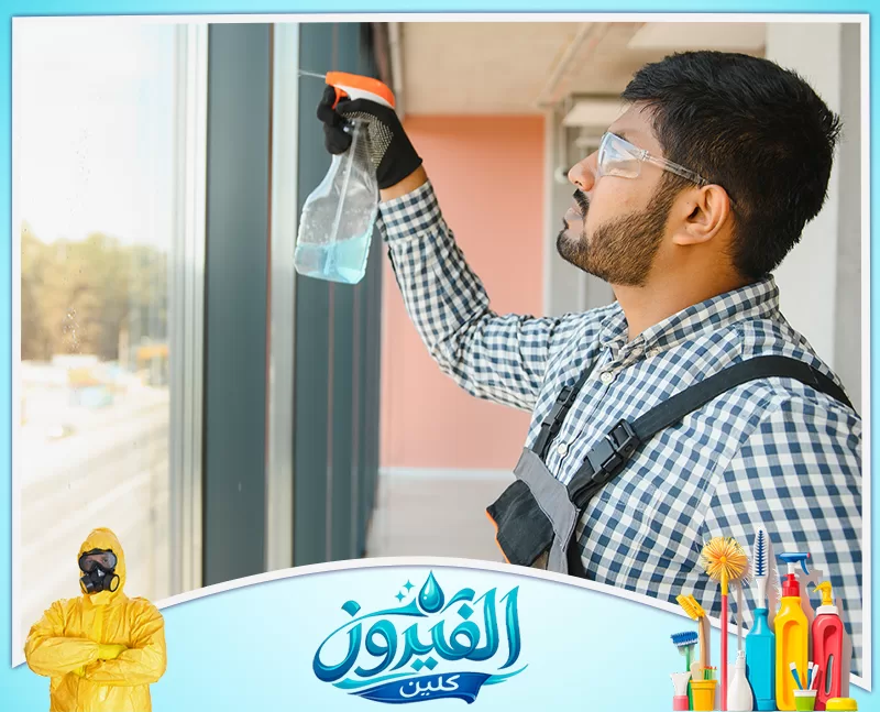 تنظيف رخام مداخل العمائر في القطيف 0562185880 شركة الفيروز عامل تنظيف يرتدي نظارة واقية وقفازًا يرش سائل تنظيف على نافذة.