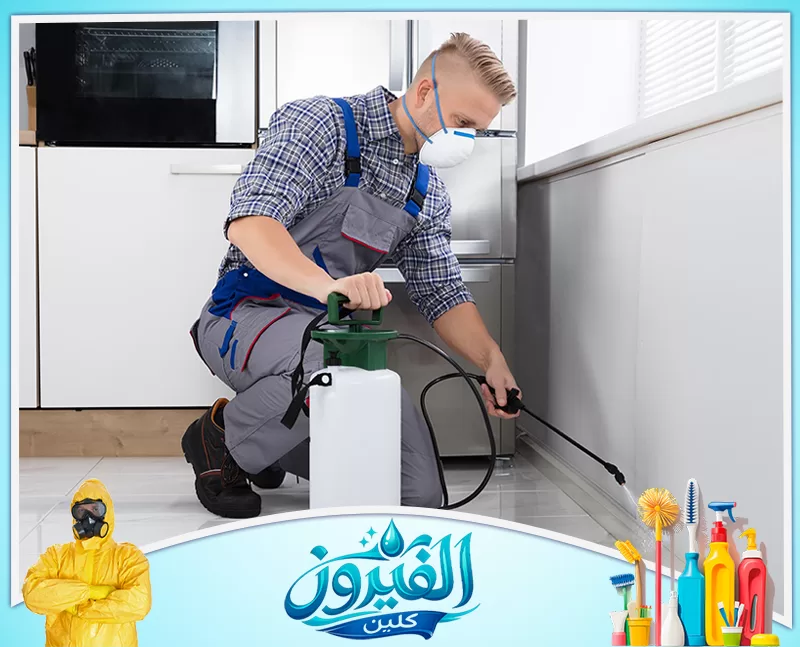 رش مبيدات بالخبر 0562185880 شركة الفيروز فني متخصص يرتدي كمامة وقائية، يقوم برش الزوايا السفلية في مطبخ حديث باستخدام مضخة ضغط للقضاء على الحشرات بفعالية.