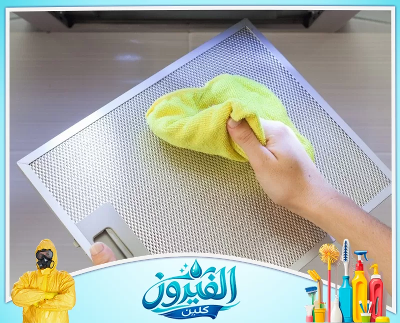 تنظيف هود المطاعم بالظهران 0562185880 شركة الفيروز يد تمسك بقطعة قماش صفراء لتمسح مرشح شفاط مطبخ معدني لامع، لضمان نظافته وكفاءته.