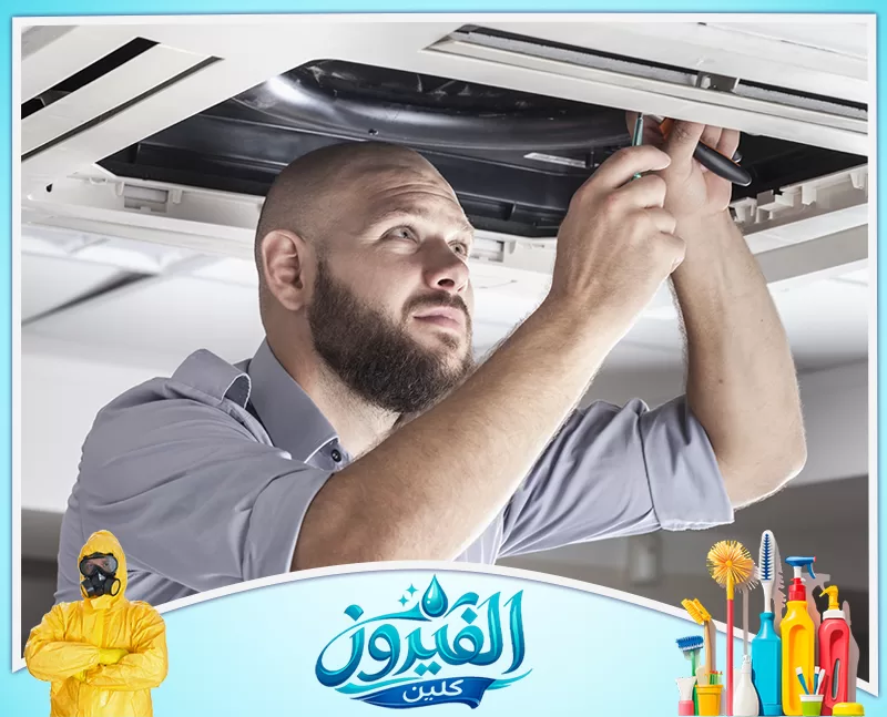 شركة تركيب مكيفات اسبليت بالظهران 0562185880 شركة الفيروز عامل صيانة ذي لحية، يرتدي قميصًا أزرق، يعمل بجد وتركيز على تصليح وحدة تكييف الهواء المعلقة في السقف