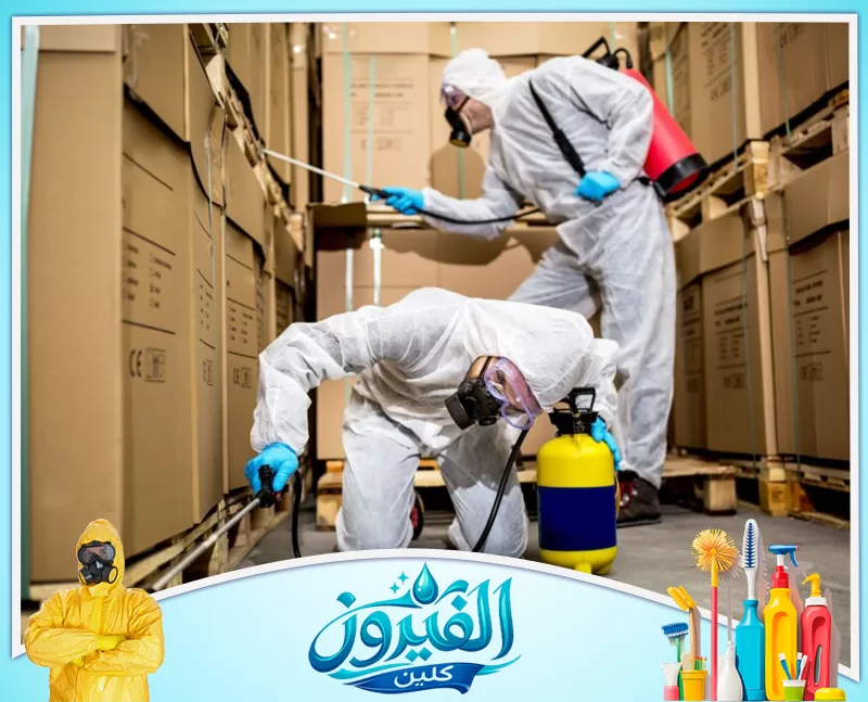 مكافحة الصراصير بالدمام 0562185880 شركة الفيروز فنيان بزي حماية كامل وأقنعة يرشون مبيدات حشرية داخل مستودع كرتون لضمان التعقيم ومكافحة الآفات