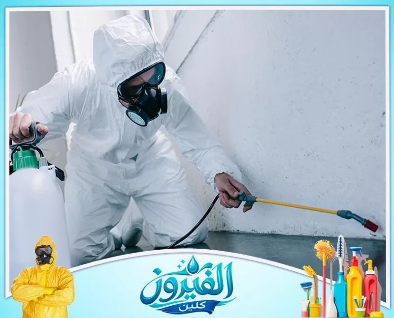 مكافحة النمل الأبيض في الدمام 0562185880 شركة الفيروز لشخص يرتدي بدلة حماية كاملة وقناع تنفس أثناء استخدام بخاخ مضغوط لرش حافة جدار، مع التركيز على عملية التطهير.