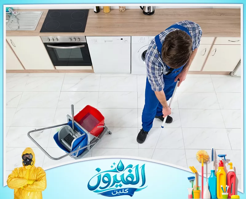 شركة تنظيف كنب بالدمام 0562185880 شركة الفيروز عامل تنظيف يمسح أرضية مطبخ بيضاء باستخدام ممسحة ودلو، مع شعار الفيروز كلين أسفل الصورة.